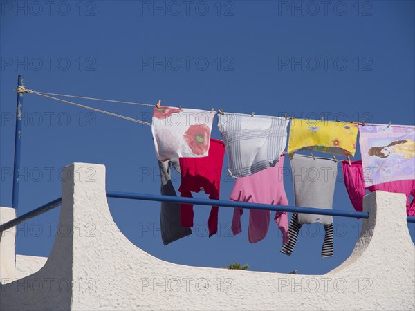 Colourful clothes hanging on a clothesline on a roof under the blue sky, The volcanic island of Santorini with blue and white houses and churches, flowers and the deep blue sea, Santorini, Greece, Europe