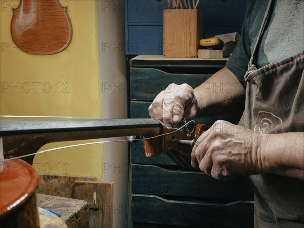 A luthier works on a cello strings in a workshop, focusing intently on string adjustments