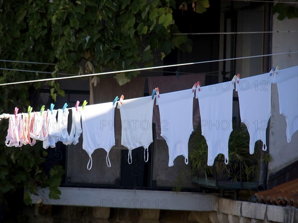 White towels hanging on a washing line, fastened by colourful clips, in the background a balcony with green plants, the old town of Dubrovnik with historic houses, churches, red roofs and fortress walls, dubrovnik, coratia