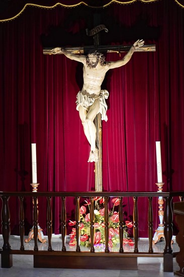 Basilica de Nuestra Senora, Candelaria, Tenerife, Canary Islands, Spain, Europe, Wooden crucifix with figure of Jesus in front of a deep red curtain, flanked by two candles on an altar, Europe