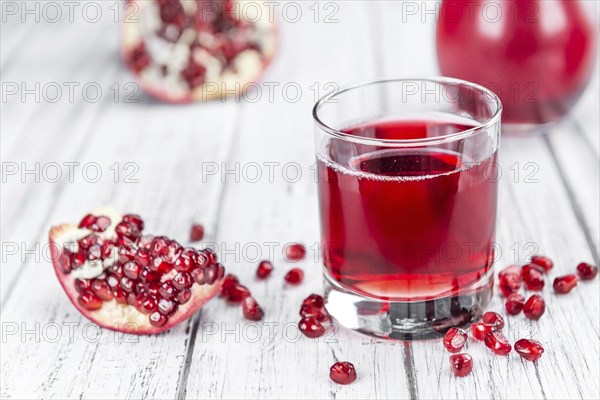 Pomegranate juice as high detailed close-up shot on a vintage wooden table (selective focus)