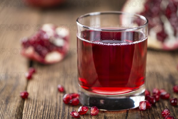 Pomegranate juice as high detailed close-up shot on a vintage wooden table (selective focus)