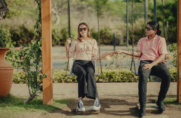 Young couple in love holding hands on a swing. Portrait of a young couple in love swinging in a nature park