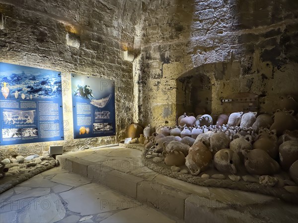 View of ancient amphorae from old historical shipwreck recovered in Mediterranean Sea wreck sunk in the sea exhibited in 16th century fortress built by Republic of Venice old name Castello Rocca al Mare today Koules in harbour of Iraklion today museum, left display board with explanation of salvage underwater by diver at underwater archaeology, Heraklion, Crete, Greece, Europe