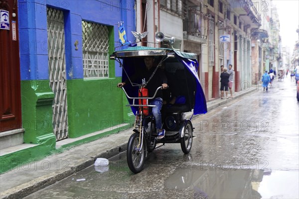 Havana, Cuba, Central America, man riding a cycle rickshaw on a wet road in an urban environment, Central America