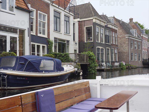 A boat moored in front of a row of townhouses on the canal on a calm, cloudy day, windows with curtains, Leiden, Netherlands