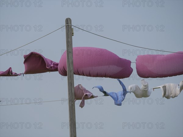 Colourful items of clothing hang on a rural washing line in the wind against the blue sky, hallig hooge, schleswig-holstein, germany