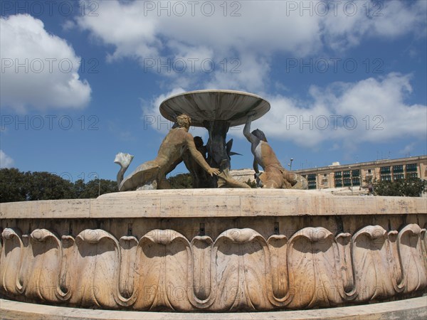 Fountain with bronze sculptures holding a bowl in front of a blue sky, valetta, mediterranean sea, malta