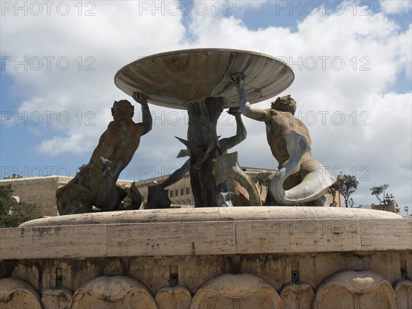 Bronze sculptures holding a large bowl of a fountain in a public square, valetta, mediterranean sea, malta