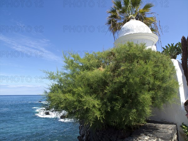 White domed tower surrounded by green plants with sea view on a sunny day, Puerto de la cruz, tenerife, spain