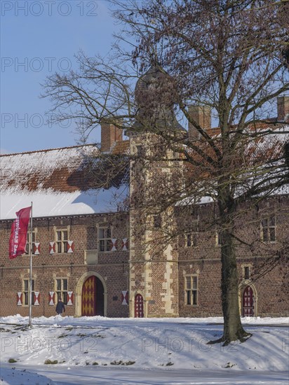 A historic castle with turrets, covered in snow and surrounded by trees with a waving flag, Raesfeld, münsterland, Germany, Europe