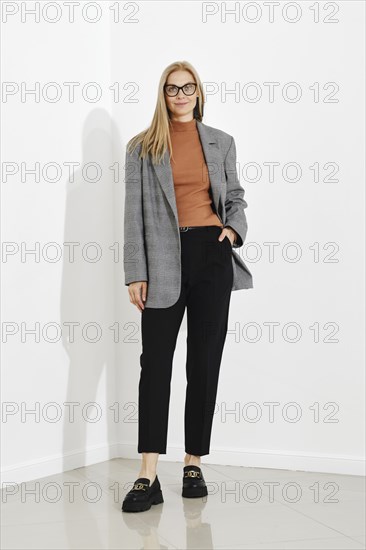 Woman in checkered jacket, brown turtleneck and black trousers posing in bright room