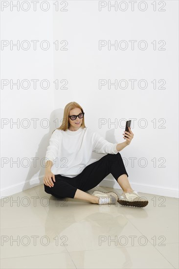 Cute woman wearing casual outfit read chat on smartphone sit on the floor against white wall