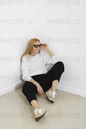 Cheerful woman in casual and comfortable clothes sits on the floor and looks to the side with her glasses raised