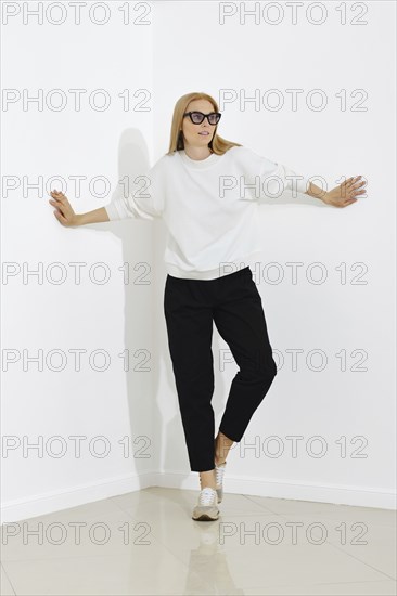 A woman in white pullover and black trousers stands in the corner with her hands against the walls