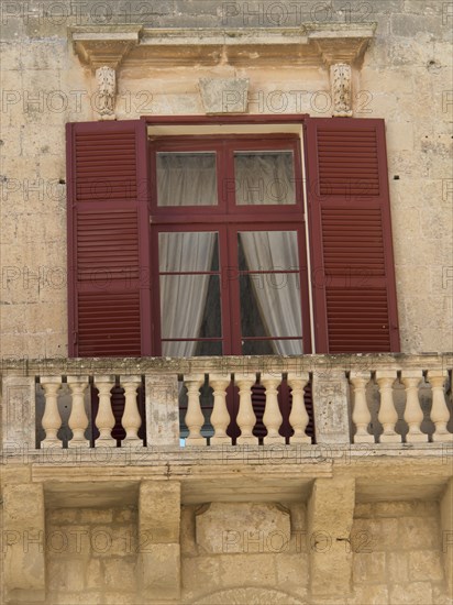 Close-up of a building with red shutters and a small balcony with opaque curtains, mdina, mediterranean sea, Malta, Europe