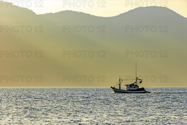 Fishing trawler sailing in front of the mountains of Ilhabela during sunset, Ilhabela, Sao Paulo, Brazil, South America