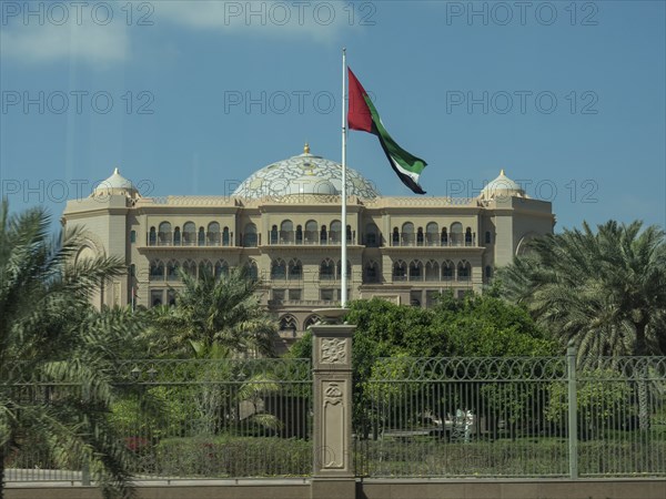 An imposing palace with a waving flag and surrounded by palm trees, abu dhabi, united arab emirates