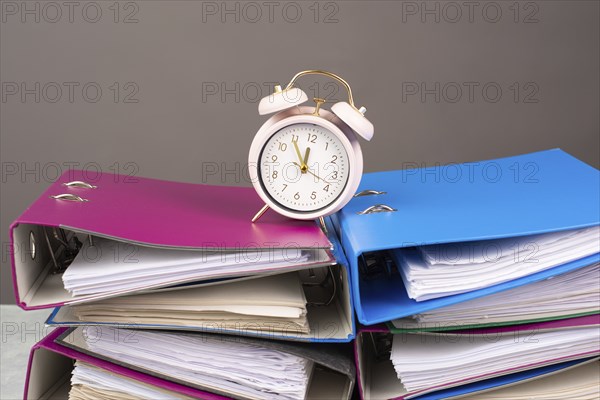 Alarm clock standing on pile of file folders, burnout, stress and overworked, pressure at work, deadline