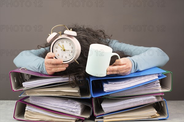 Exhausted tired woman with coffee and alarm clock, pile of file folders, burnout, stress and overworked, pressure at work