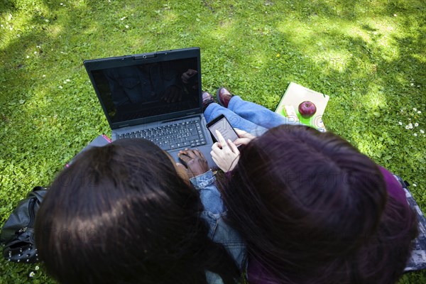 Multiracial couple of women using laptop and cell phone at the park. Lifestyle concept