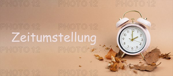 Alarm clock with autumn foliage, end of daylight saving time in fall, winter time changeover stands in german language beside the clock