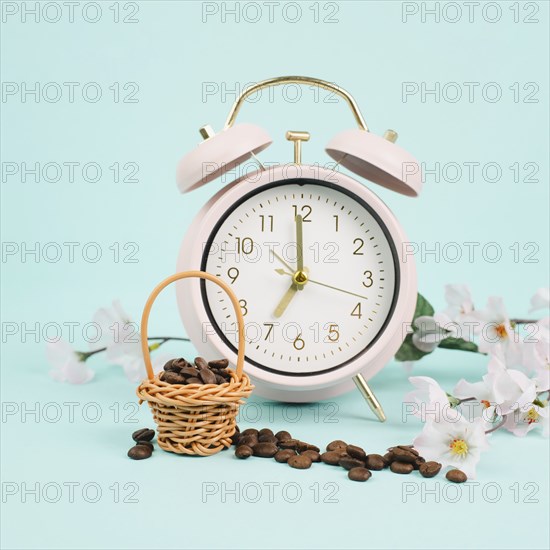 Wicker basket with roasted coffee beans, an alarm clock and cherry blossom, wake up in the morning, spring season