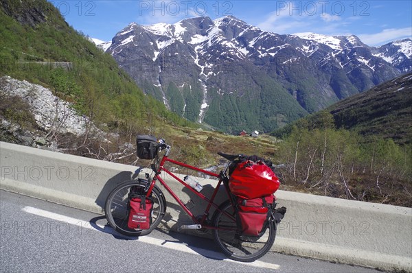 Packed bike on a road in front of snow-covered mountains, a perfect adventure picture in Norwegian nature, Gaularfjell, pass road, Norway, Europe