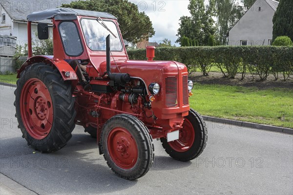 Red vintage tractor, carefully restored oldtimer, driving on the road through the village, motion bluer, selected focus