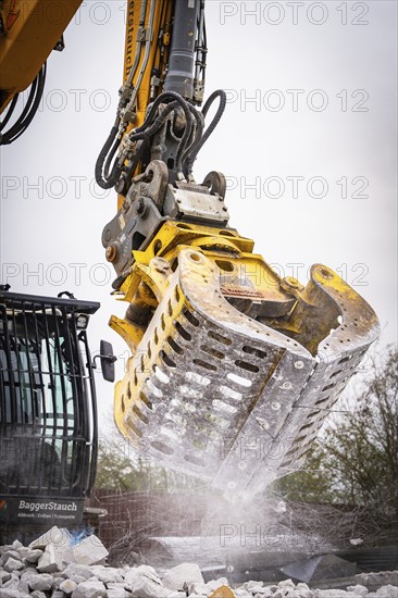 Yellow excavator with a massive metal grab cleans debris on a construction site, water splashes out, demolition site, Saarbrücken, Germany, Europe