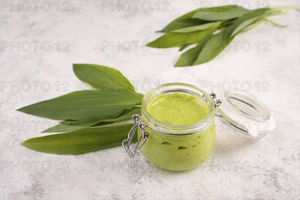 Pesto made from wild garlic, pine nuts and feta cheese in a glass, with fresh leaves on a textured background, empty space for text