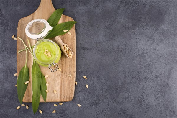 Pesto made from wild garlic, pine nuts and feta cheese in a glass, with fresh leaves on a dark textured background, empty space for text