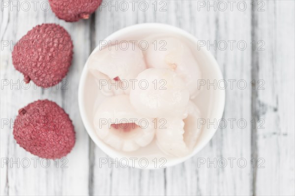 Lychees (preserved) as high detailed close-up shot on a vintage wooden table (selective focus)