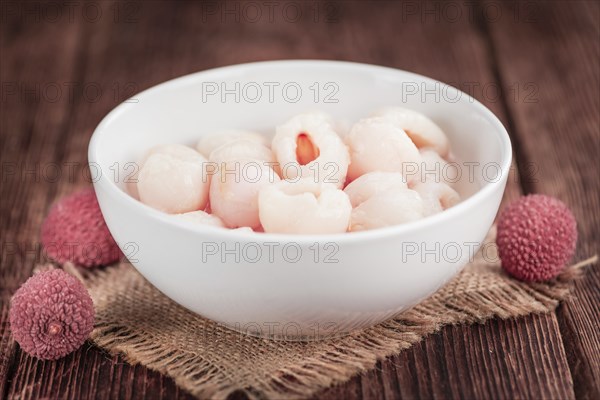 Lychees (preserved) as high detailed close-up shot on a vintage wooden table (selective focus)