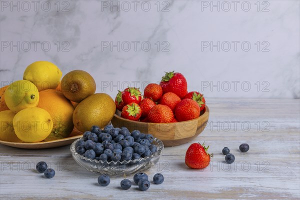 Harmonious still life of various fruits, strawberries, lemons, oranges, kiwis and blueberries on wood against a marble background