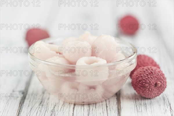 Lychees (preserved) as high detailed close-up shot on a vintage wooden table (selective focus)