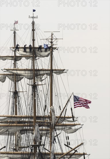 New London, Connecticut, USA, July 2012: Crew members high up in the rigging furl the sails on the US Coast Guard cutter Eagle when it arrives at Fort Trumbull, New London, Connecticut at the conclusion of the Parade of Sail during Operation Sail 2012 aka OpSail 2012. New London is the Eagle's homeport. Originally a German vessel, the ship was built in 1936 by the Blohm and Voss Shipyard in Hamburg, Germany. The square rigger is a training vessel for US Coast Guard cadets. While underway, the Eagle's crew must handle more than 22, 000 square feet of sail and five miles of rigging, North America