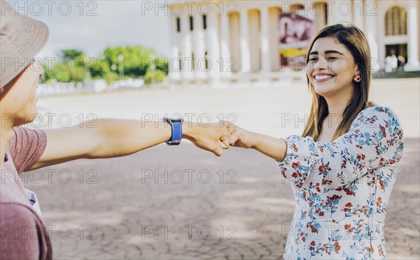 Two young smiling teenagers bumping fists in the street. Close up of guy and girl shaking fists in the street