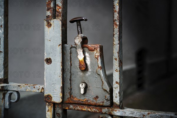 Nostalgic rusty door lock with a modern lock cylinder on a metal entrance grille, copy space in the dark background, selected focus