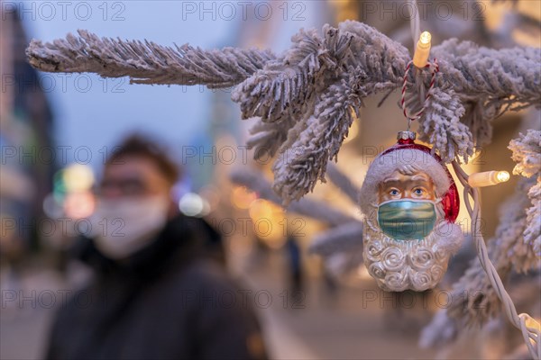 Symbolic picture Christmas in the Corona crisis, Father Christmas figure, Christmas tree decoration, with mouth-nose mask, everyday mask, in a pedestrian zone, shopping street