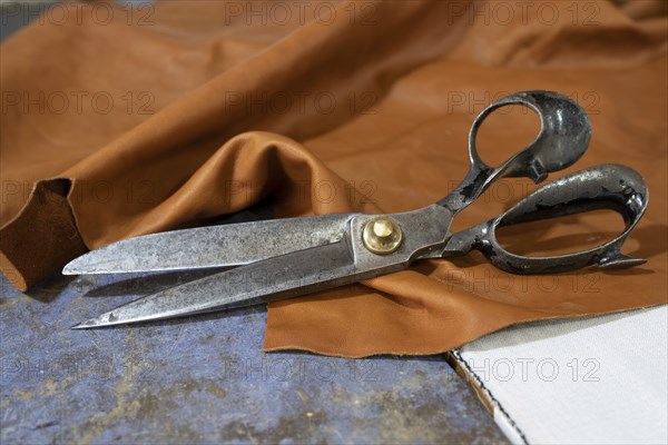 Big old scissors lying on a piece of leather in a craft workshop, copy space, selected focus, narrow depth of field