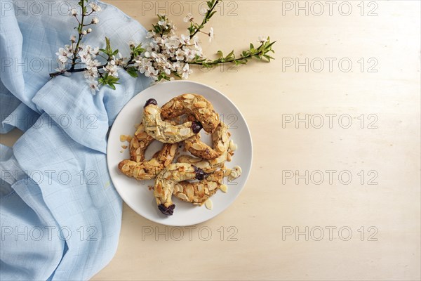 Almond crescent cookies on a plate, spring flower branch and blue napkin on a light wooden table, large copy space, high angle view from above