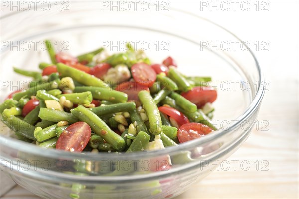 Salad of green beans, tomatoes, pine nuts and feta cheese in a glass bowl on a light wooden table, Mediterranean antipasto, copy space, selected focus, narrow depth of field