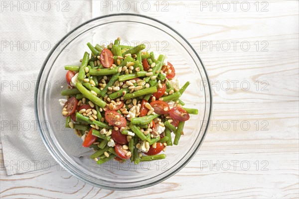 Antipasto salad of green beans, tomatoes, pine nuts and feta cheese in a glass bowl on a light wooden table, copy space, high angle view from above