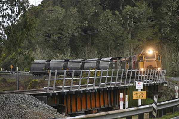 NGAHERE, NEW ZEALAND, SEPTEMBER 2, 2019: A small coal train turns the corner to cross the bridge at Ongionui Creek near Ngahere on the West Coast of New Zealand