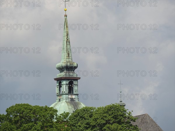 Detail of a church tower in front of a cloudy sky with green trees in the foreground, Kappeln, Schleswig-Holstein, Germany, Europe