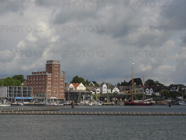 Buildings and boats along a coastline under a cloudy sky, Kappeln, Schleswig-Holstein, Germany, Europe