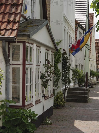 Simple residential buildings with floral decorations and a flag along a cobbled street, Kappeln, Schleswig-Holstein, Germany, Europe