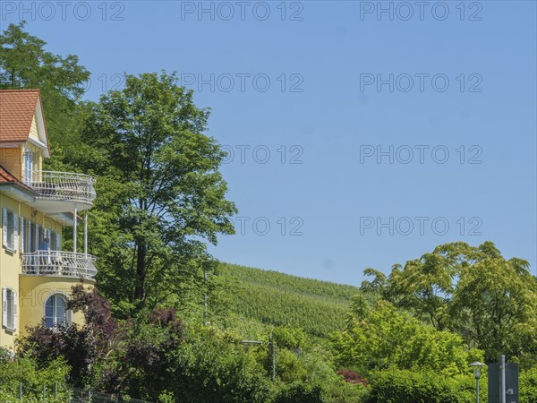 A house with balconies and green shutters, surrounded by lush trees and hills under a cloudy sky, Meersburg, Lake Constance, Germany, Europe