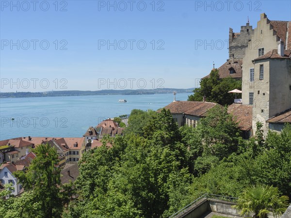 A castle and surrounding buildings on the lakeshore with lush greenery and red roofs, Meersburg, Germany, Europe